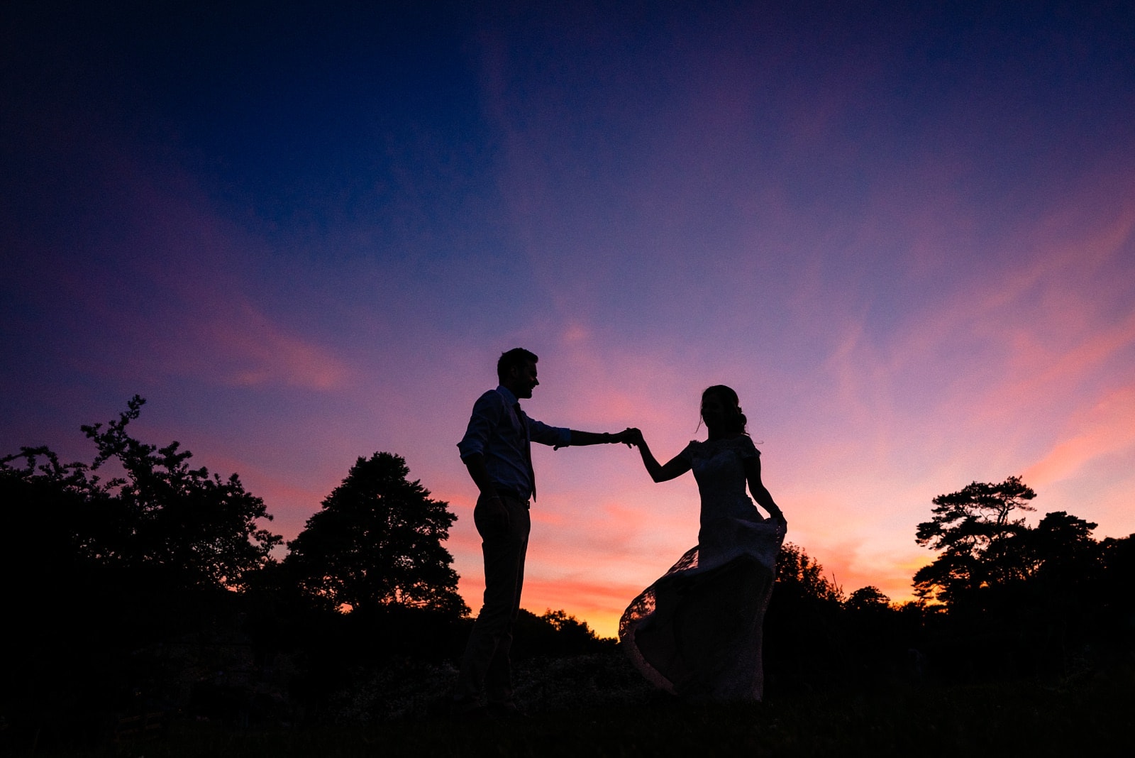 Silhouette of a bride and groom on their wedding day at Nancarrow Farm, in front of a purple sunset.