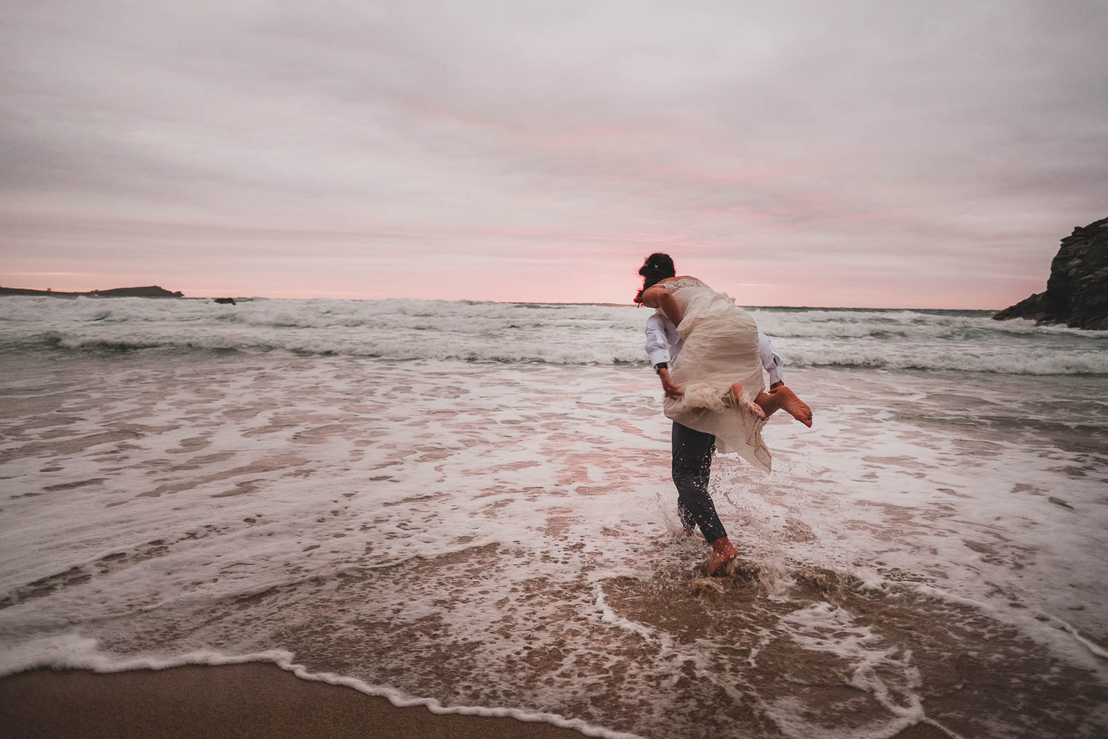 A portrait of a bride/groom going in the sea at Lusty Glaze beach.