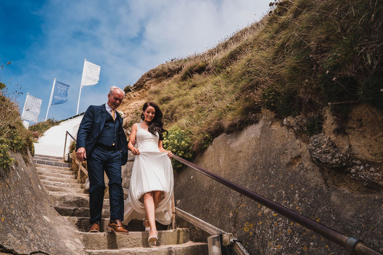 A bride and her Dad walk down the steps to Lusty Glaze beach for the wedding day.